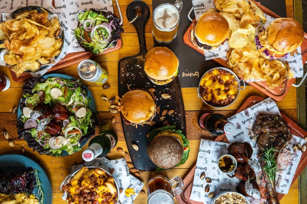 multiple burgers, chips, fries, and other junk food on a table