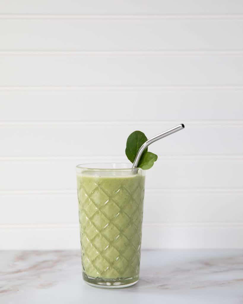 a green smoothie with a stainless steel straw in a clear glass
