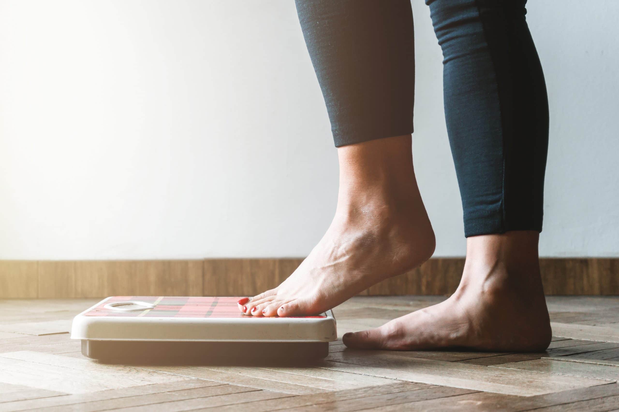 A woman steps on a scale to track her healthy weight loss progress