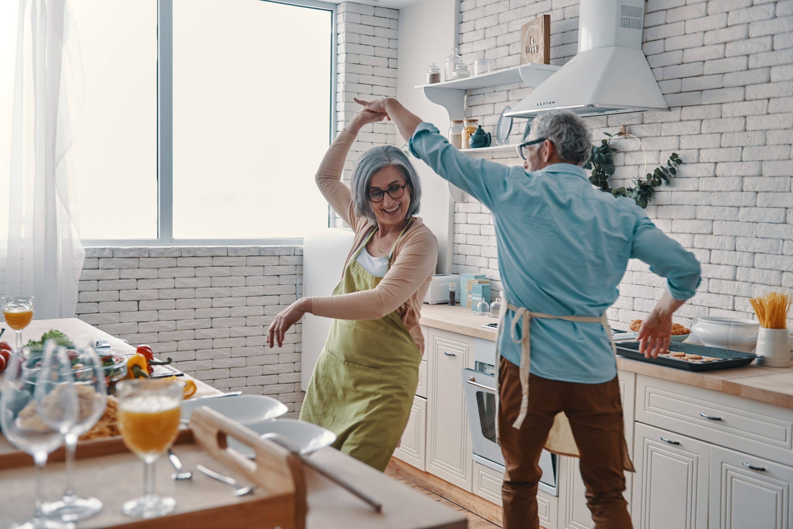 A woman dances joyfully with her husband in a white kitchen. Bioidentical hormones restore energy and vitality.