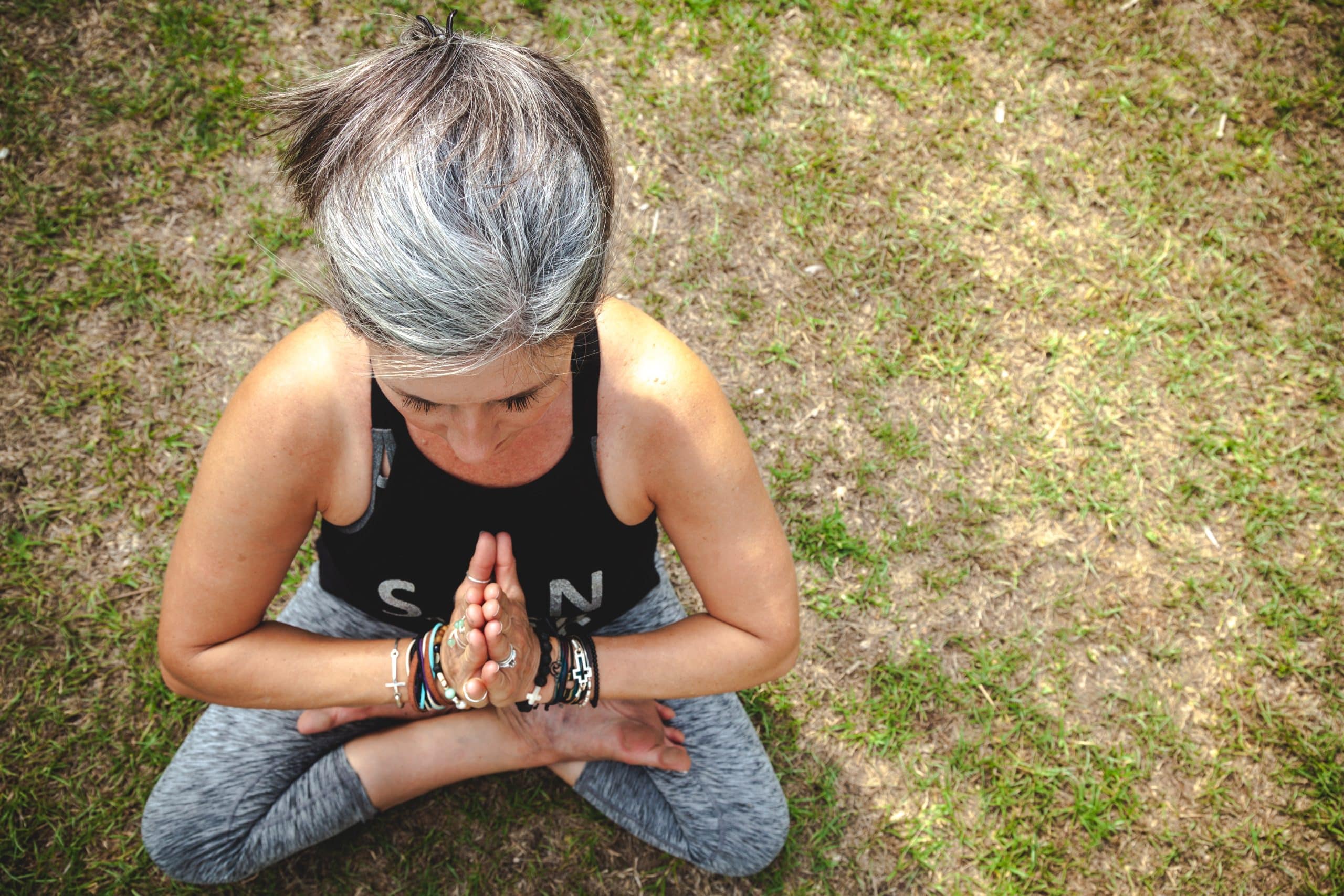 Top-down view of a woman with graying hair sitting in a yoga pose on the grass, symbolizing hormone balance