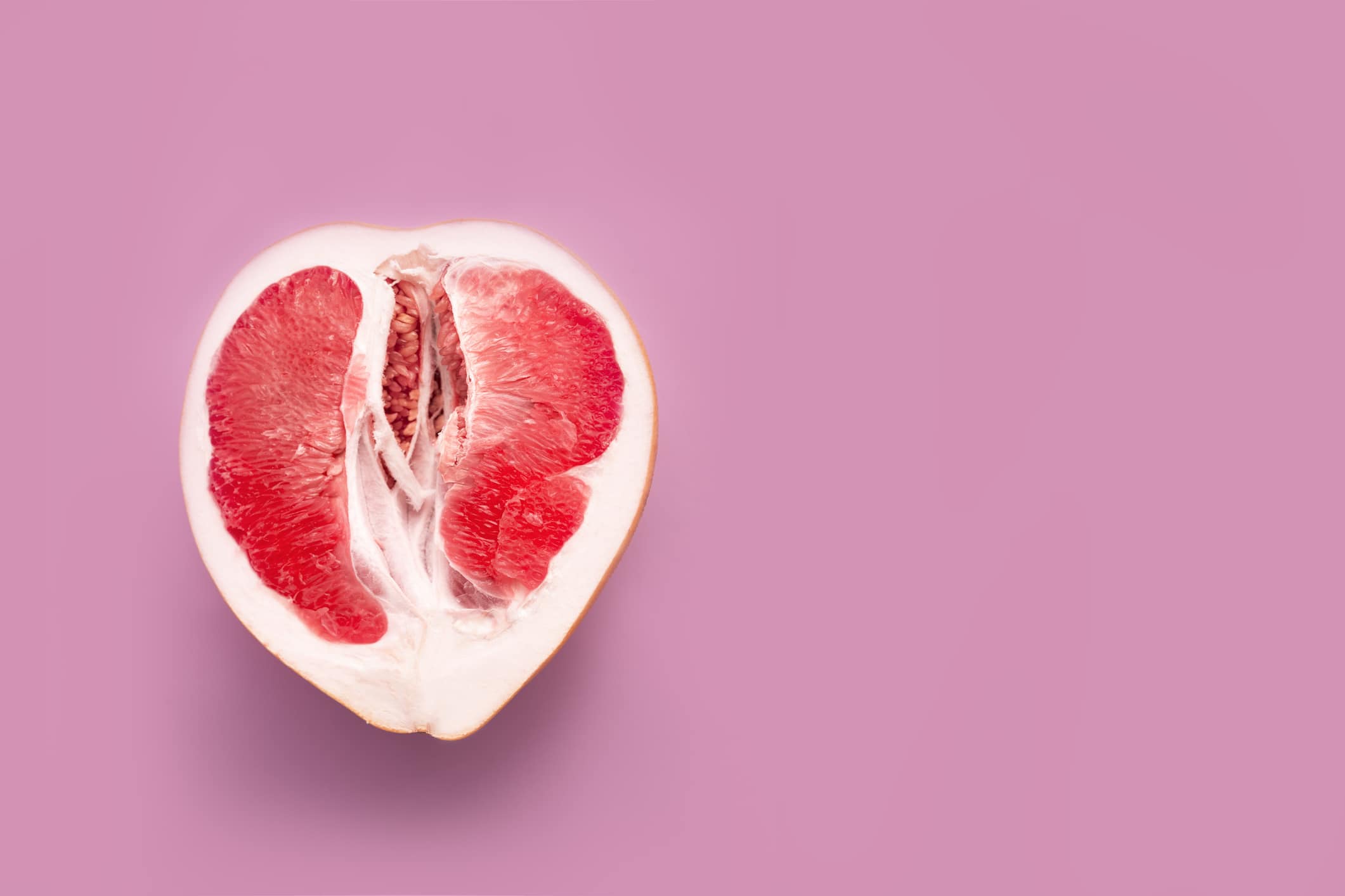 A halved grapefruit representing the female reproductive system on a pink background.