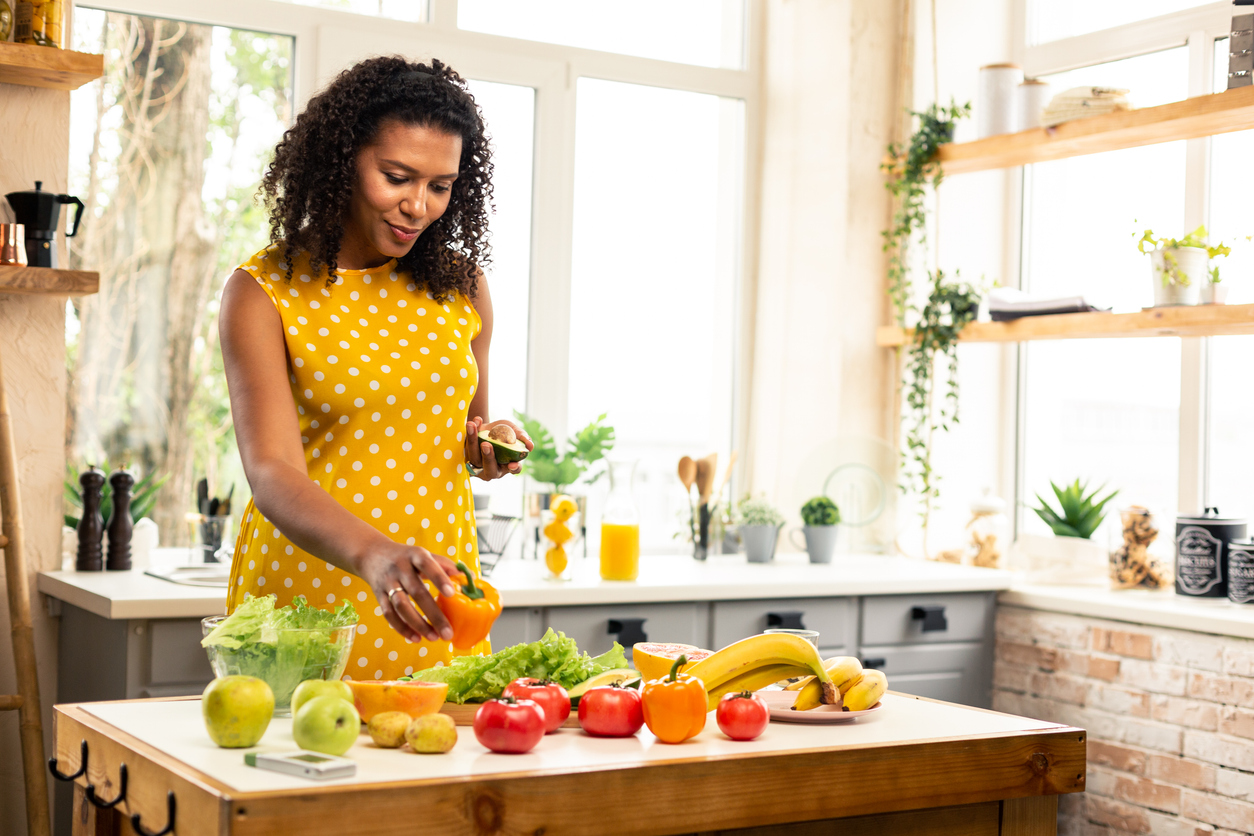 An expectant mother preparing a meal with vegetables in her kitchen.