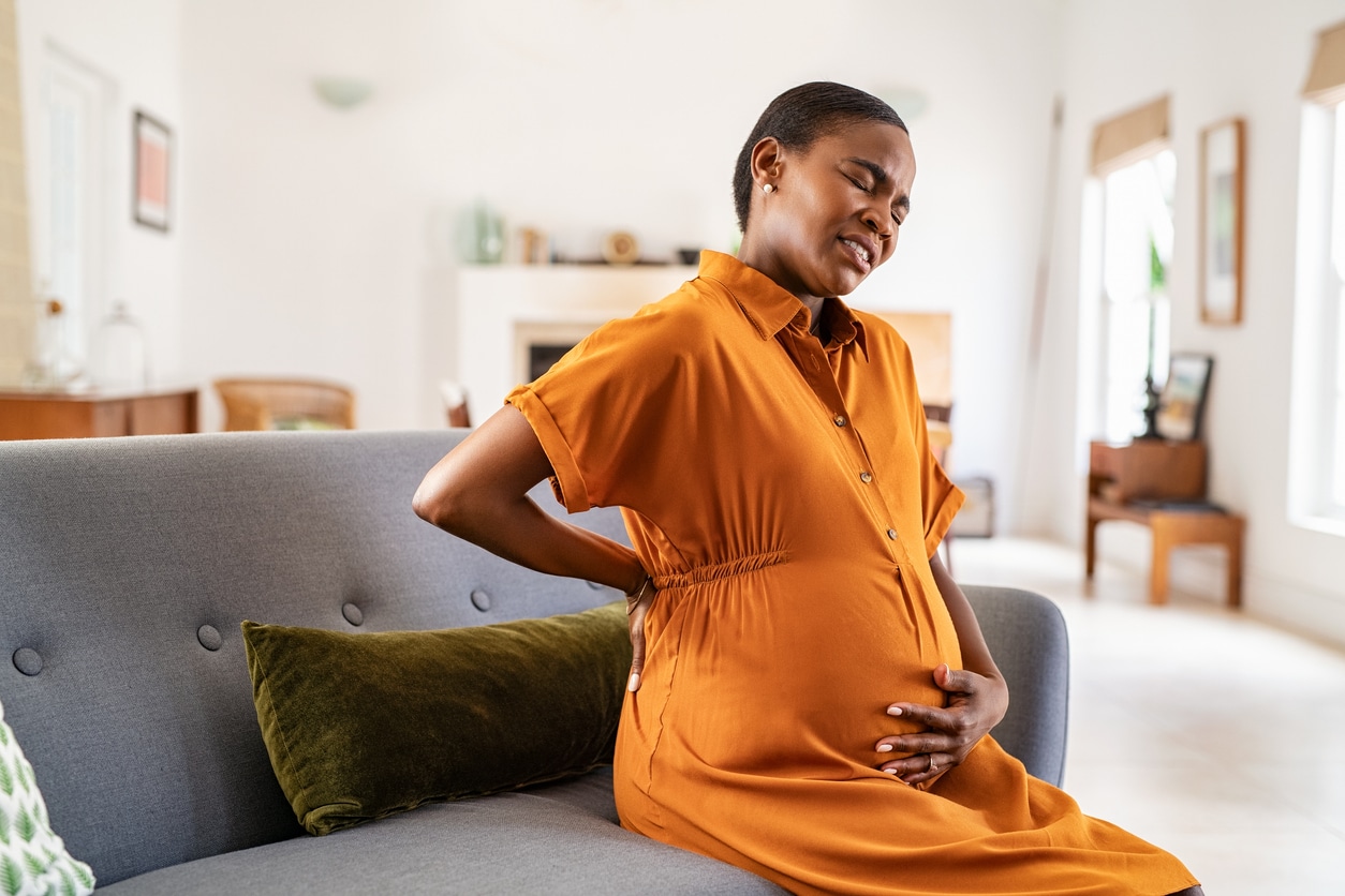 A pregnant woman holding her back as she suffers from pain.